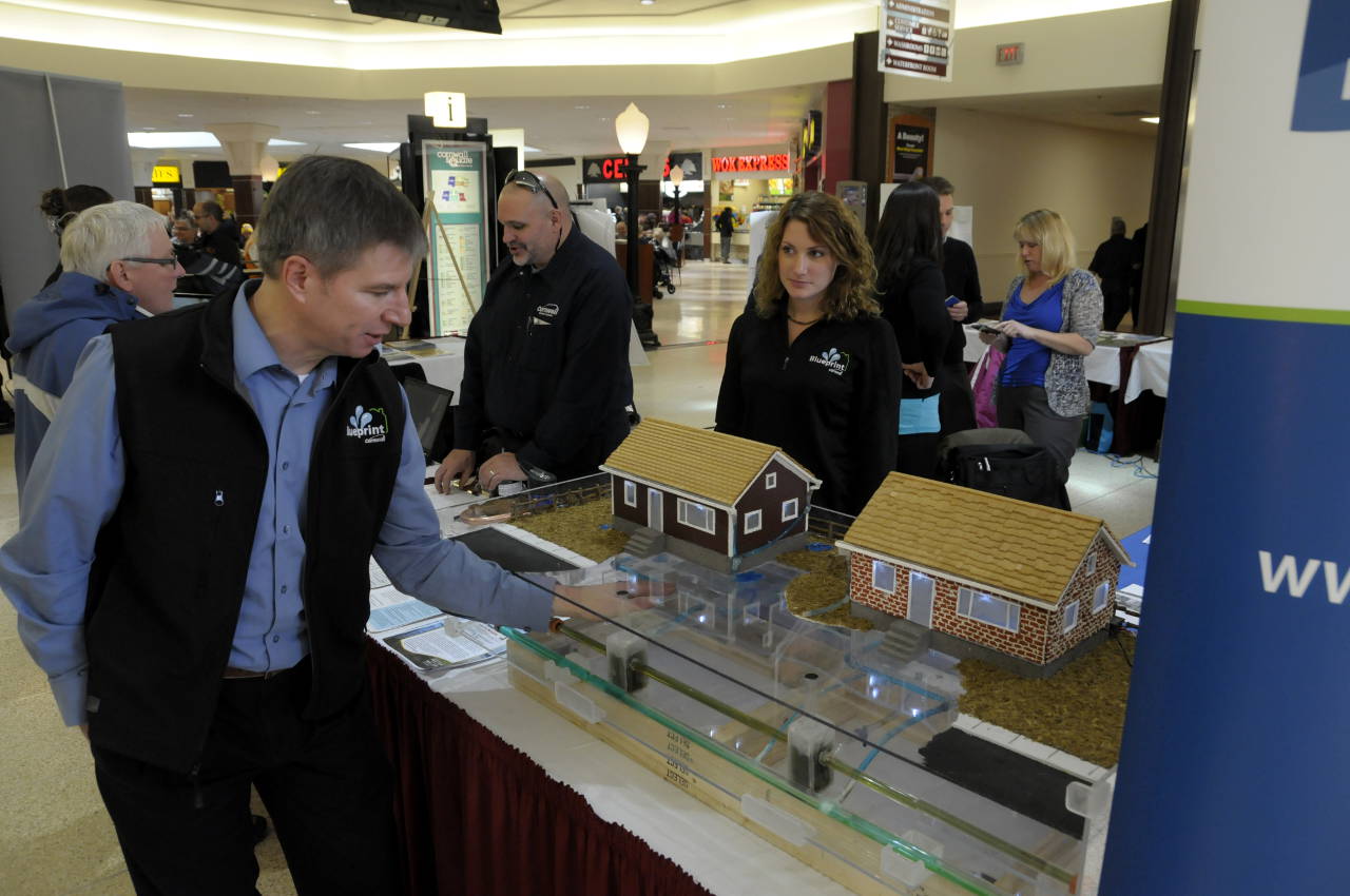 City of Cornwall Infrastructure GM John St. Marseille shows off a model illustrating how changes under the flood rebate program will improve water flow for the city and the homeowner. Flood rebate coordinator Tracy Gordon (right) watches the presentation. (Cornwall Newswatch)