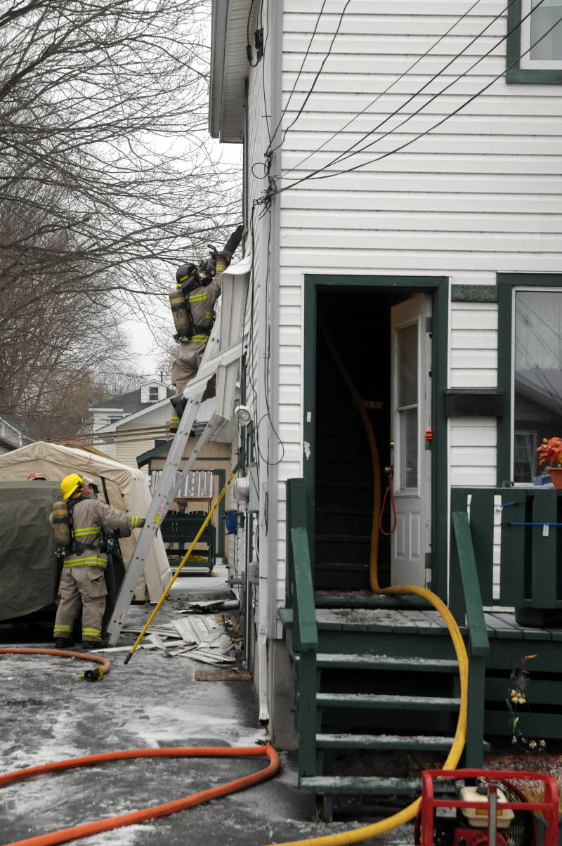 A Cornwall firefighter readies his chainsaw while another holds the ladder. The fire department was trying to put out a fire in a wall of this home on Eighth St. W on Dec. 6, 2014. (Cornwall Newswatch/Bill Kingston)