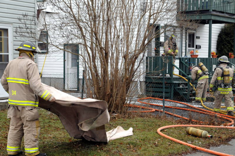One firefighter, left, gets a blanket ready to lay down their equipment while three others, right, get their breathing gear ready to enter the home. The duplex on Eighth St. West had a fire in a wall on Dec. 6, 2014. (Cornwall Newswatch/Bill Kingston)