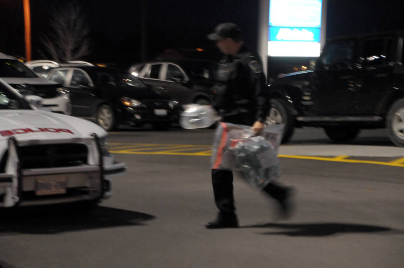 Cornwall police Const. Justin Wheeler carries evidence bags to his cruiser Dec. 10, 2015 from Menchie's on Ninth Street East in Cornwall, Ont. Police and firefighters were called to a report of a suspicious package, which has been seized for further testing. (Newswatch Group/Bill Kingston)