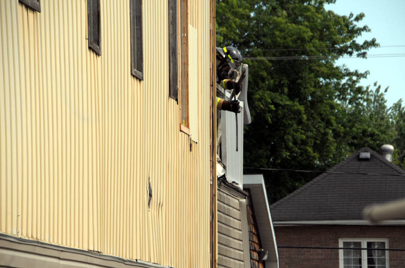 A Cornwall firefighter tears away part of a deck and siding on the back of a strip mall Friday, July 8, 2016 after a fire, likely caused by smoking. The damage was contained to the outside of the City Center at 812 Pitt Street. (Newswatch Group/Bill Kingston)